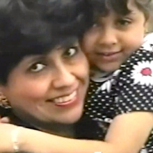 A mom and her daughter embrace in a close up of their faces, the little girl wearing a black and white polka dot dress. 