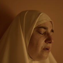 Still from 'Q.' Eyes closed, Hiba's face is softly lit against a light background, with a tear streaming down her cheek.