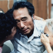 A middle-aged Korean man embraces two older Korean women as they cry