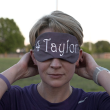 Close up of a woman with short, blonde hair wearing a blindfold that reads "4 Taylor"