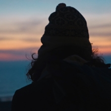 Film still from 'Your Friend Memphis': the silhouette of a person's back, as they look out to a sunset over the ocean.