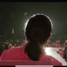 A woman wearing a pink top with black hair shot from the back. She is front-lit.