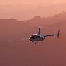 A helicopter is flying past the hazy silhouettes of the Hollywood Hills in a pink sunset.