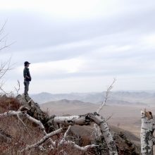 In the distance, a young man stands on the edge of a mountain and looks across a wintery valley.