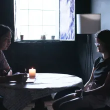 Two figures sit at a small round table, which has a candle on it.