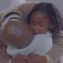 Two Black people are embracing in a close hug.