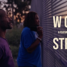 Two black men stand at a fence. Text on the right side of the image reads: Wood Street, a feature documentary.