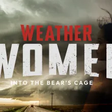 Dominated by a looming supercell thunderstorm over an open rural road, the image shows a lone vehicle driving straight into the heart of the storm. Bold, distressed white typography spells out “WOMEN,” anchored by a sharp red “WEATHER"
