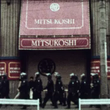 Film still showing a line of police walking down a public street.