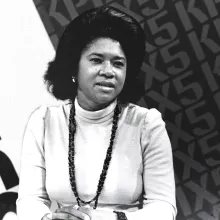 A black and white photograph of a woman with dark hair wearing a white top.