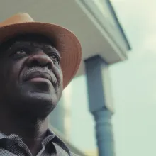 A Herero man wearing a straw hat looking beyond his front porch.