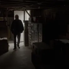 A man is silhouetted as he enters a basement filled with file cabinets and boxes.