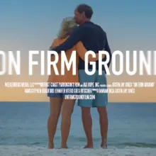 A couple faces the ocean in an embrace, the man holding his wife and kissing her head. The title "ON FIRM GROUND" over the image.