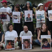 Two rows of people stand in silent vigil outside, holding large print-out posters of children's faces.