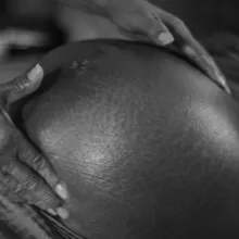 Black and white image of a pregnant woman's belly with the midwive's hand gently holding it.