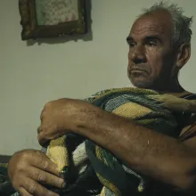An older man holding a stork in a blanket in his living room.