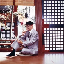 Osamu Tezuka (c. 1973) sits on the floor in a traditional Japanese room, observing a drawing, with a brush in his hand.