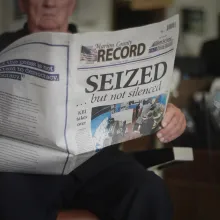 A man holds a newspaper with the headline: "SEIZED."