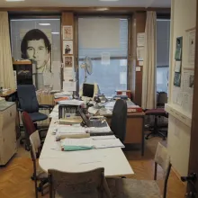 An empty, cramped office with plenty of strewn papers and posters covering every wall