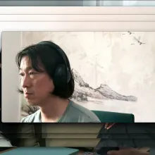 The image of a middle-aged Asian man with long black hair parted in the middle wears headphones and a light green t-shirt hovers over a repeated image of two people sitting on a green couch