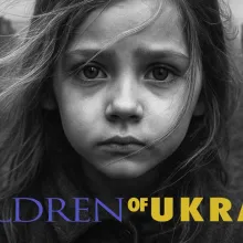 A wide, panoramic film poster featuring a young person's face in a close-up, central position. The person has light-colored hair that appears windblown and a serious, direct gaze. The background consists of desaturated, out-of-focus ruins of buildings, suggesting a scene of significant destruction.  Across the bottom of the image, the title "CHILDREN OF UKRAINE" is displayed in large, bold capital letters. The words "CHILDREN OF" are in dark blue, and the word "UKRAINE" is in a bright yellow. To the far lef