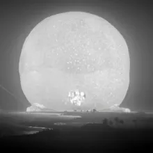 Black and white shot of a large beam of light mushrooming following an atomic bomb