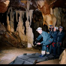 Three middle-aged white men in gear and holding cameras pose for a photo inside a cave lit only by the flash of the camera