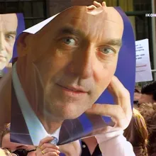 A poster of a white bald freshly-shaven man is being held up by a crowd