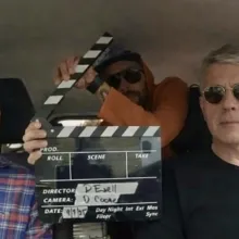 A candid production still showing three members of the Paper Moon Rise team inside the car used during their Kansas road journey. Seated on the left is on-screen talent Harry Cooke, in the center is Director of Photography David Coone holding the film slate, and on the right is producer/director David Ezell at the wheel. The image captures the spirit of a small crew on the road, documenting the landscapes and communities at the heart of the film.