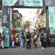 Wide shot of an open street adorned with Kolkata People's Festival banners with various people milling around