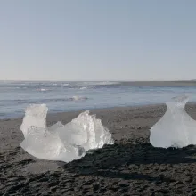 Two pieces of ice are seen melting on a sandy beach