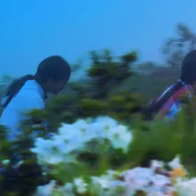 Wildly saturated photo of two young girls with long black hair walking in a meadow filled with flowers