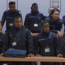 14 uniformed guards stand in two rows behind long tables