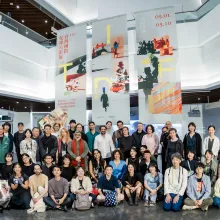 50 people of varying ages and races stand and kneel in three rows in a large, open exhibition space. Three large banners behind the group read "Taiwan International Documentary Festival 2026"