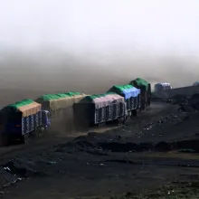 A line of covered trucks drive over black terrain