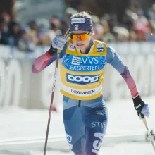 A blonde woman in a ski uniform, goggles, and headband skis furiously