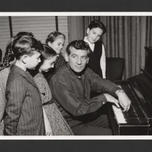 Leonard Bernstein playing the piano with a group of young children.