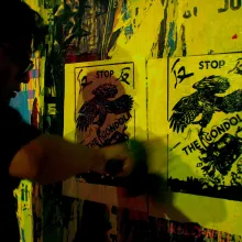 A shadowy figure wheatpastes a flyer on a wall.