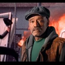 A Black man stands in front of an inflamed car, from Melvin Van Peebles' 'Classified X.' 