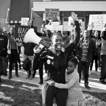 A Black woman with a megaphone raises her arm and shouts in a crowd of people. From Sabaah Folayan's 'Whose Streets?', a Magnolia Pictures release. Photo courtesy of Magnolia Pictures.