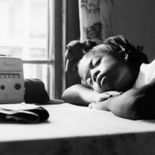 Black-and-white image of a young Black girl listening to the radio with her eyes closed. From Garrett Bradley’s ‘America.’ Courtesy of Museum of Modern Art