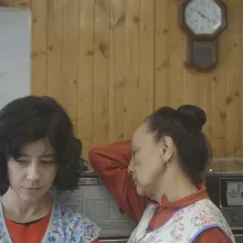 Two female laundry workers are wearing floral aprons and standing against a wooden wall. From Lynne Sachs’ ‘The Washing Society.’ Courtesy of The Criterion Channel. 