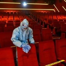 Person in a hazmat suit cleaning a seat inside of an empty movie theater. 