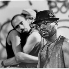 Marlon Riggs is a Black male filmmaker seen here in an archival black and white image from his film 'Tongues Untied.' He is wearing a leather vest and a hat. Courtesy of the Criterion Collection.