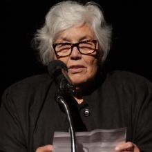 Lourdes Portillo, a Latinx woman with white hair, glasses and a black top, accepting the IDA Career Achievement Award in 2017; Portillo is the only filmmaker to have earned IDA Documentary Award in four different decades. Photo: Susan Yin