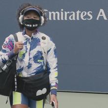 Tennis player Naomi Osaka, an Afro-Japanese female tennis player on a tennis court wearing a multi-colored jacket, and a mask that says “Tamir Rice.” Still from Garrett Bradley’s Netflix series, ‘Naomi Osaka’. Courtesy of Netflix