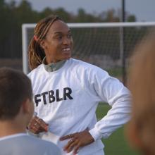 Soccer player Jessica McDonald is a Black woman in her 30s. Here, she is wearing a white shirt that says “FTBLR” and her hair is tied back. Image from Andrea Nix Fine and Sean Fine’s ‘LFG.’ Courtesy of HBO Max 