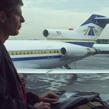 Profile of Anthony Bourdain, a white man in a jacket, against blue and white stationary airplanes. Still from Morgan Neville’s ‘Roadrunner: A Film About Anthony Bourdain.’ Courtesy of Cinetic Media.