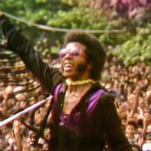 Sly Stone, a Black male musician in violet and black, plays to a huge crowd in Questlove’s ‘Summer of Soul’ (Director: Questlove; Producer: David Dinerstein, Robert Fyvolent, Joseph Patel) Courtesy of Cinetic Media.