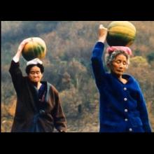 Two older women walk while balancing squash on their head, from 'Habitual Sadness.'